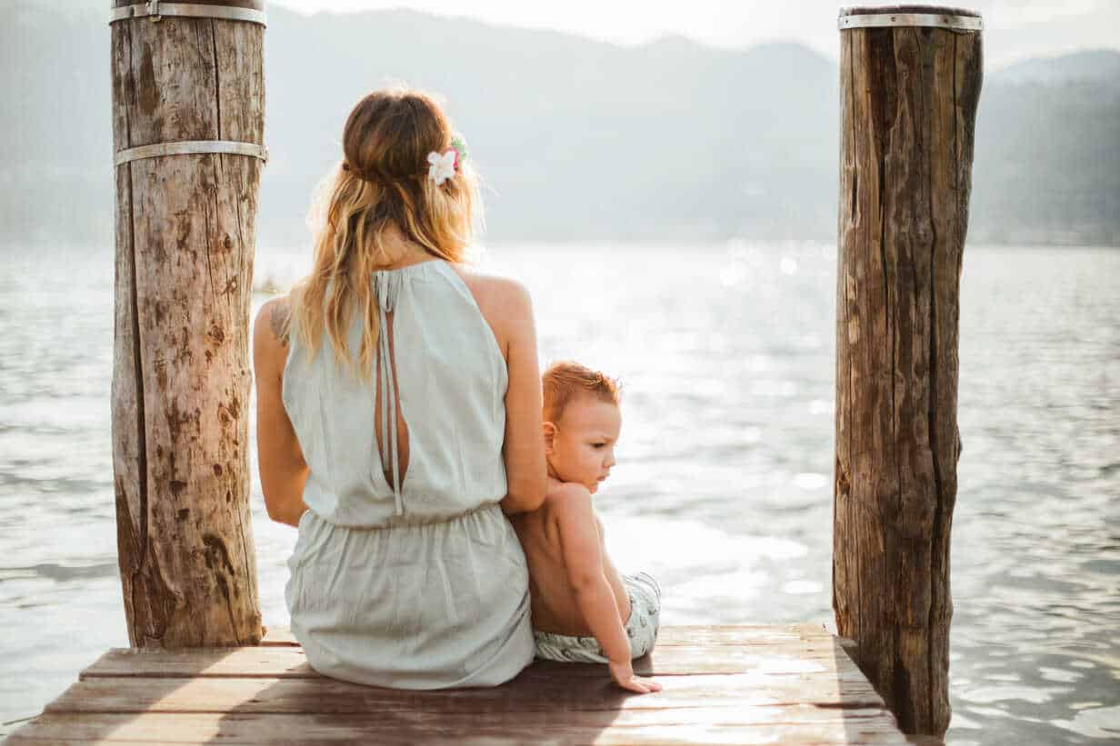 Mother and toddler son sitting on pier, rear view, Lake Orta, Piemonte, Italy